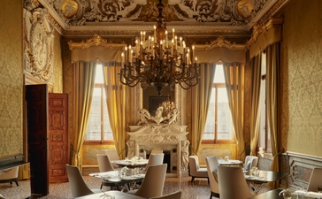 Ornate palazzo dining room at Aman Venice with gilt details, crystal chandelier, and draped windows overlooking the Grand Canal.