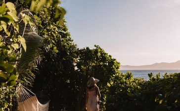 Shaded beachfront seating area at Amanpulo resort, Philippines, with tropical foliage and calm waters beyond.