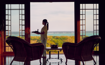 Amanpulo resort spa relaxation room with seated figure gazing towards coastal landscape through open doors.
