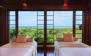 Sala de tratamientos de bienestar en Amanpulo, resort en Filipinas, con dos camas y vistas al jardín.