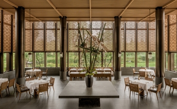 Arva restaurant at Amanyangyun, Shanghai, with floor-to-ceiling windows overlooking gardens and dining tables set with white linens.