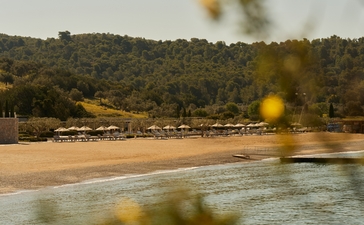 Amanzoe beach club overlooks a sandy shoreline and calm waters along the Greek coast.