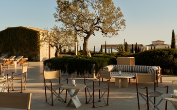 Nama Lounge exterior at Amanzoe with dining tables at dusk, overlooking the Peloponnese landscape.
