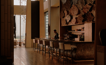 曼谷奈乐安缦酒店的酒吧，木质吧台和高脚凳沿墙排列，温暖灯光照亮室内。