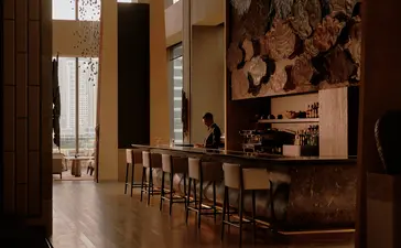 Bar area at Aman Nai Lert Bangkok with wooden counter, stools, and warm lighting.