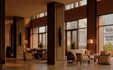 Warm-toned bar at Aman Nai Lert Bangkok with floor-to-ceiling windows, wooden furnishings, and lounge seating.