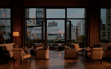 曼谷奈乐安缦酒店的露台区，配有皮革座椅和落地窗，俯瞰城市天际线。