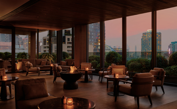 Aman Nai Lert Bangkok lounge at dusk, with floor-to-ceiling windows overlooking the city skyline and candlelit seating areas.
