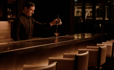 Warm-lit lounge bar at Aman Nai Lert Bangkok with wooden seating and intimate ambiance.