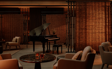 Aman Nai Lert Bangkok lounge with grand piano, warm wood panelling and comfortable seating.