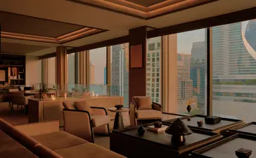 曼谷奈乐安缦酒店套房内，木质框架落地窗俯瞰城市景观，配有米色扶手椅和低调家具。