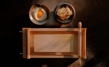 Wooden bar counter with two amber-coloured glass vessels suspended above against a dark background at Aman Nai Lert Bangkok.