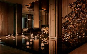 Candlelit spa sanctuary at Aman Nai Lert Bangkok, with warm golden lighting and wooden architectural details.