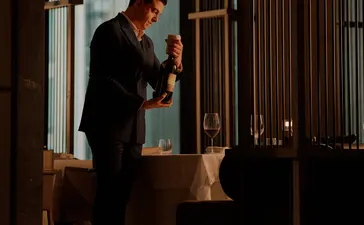 曼谷奈乐安缦酒店内，一位客人在玻璃门廊中驻足，周围环绕着木质装饰元素。