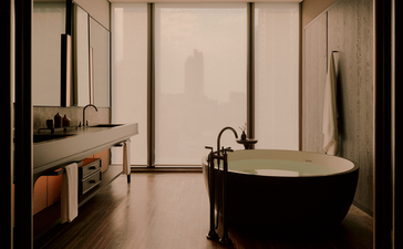 アマン ナイラート バンコクのホテルの客室バスルーム。黒い浴槽と木製洗面台、大きな窓が特徴。