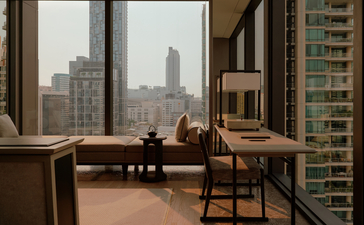 アマン ナイラート バンコクのホテル客室167番。大きな窓からバンコクの街並みが見える、木製デスクと椅子のある落ち着いた空間。