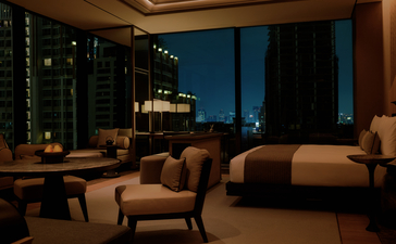 アマン ナイラート バンコクのホテルルーム167、夜間の室内。床から天井まで届く窓から夜景が見え、ベージュのソファとアームチェアが配置されている。