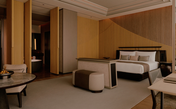 Room 169 at Aman Nai Lert Bangkok features a principal bedroom with warm wood panelling, neutral furnishings and adjoining sitting area.