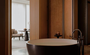 Freestanding black bathtub in a principal bedroom at Aman Nai Lert Bangkok, with wooden panelling and view to adjoining room.
