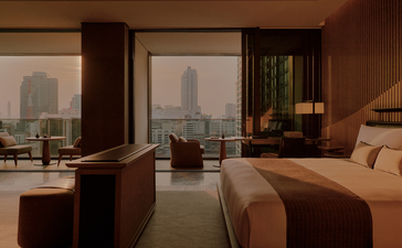 Hotel room at Aman Nai Lert Bangkok with twin beds, work desk, and Bangkok skyline views through floor-to-ceiling windows.