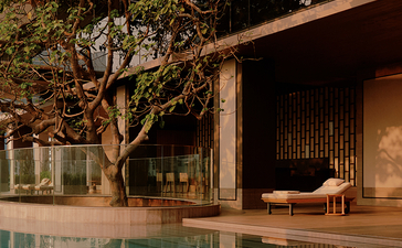 Swimming pool at Aman Nai Lert Bangkok at dusk, with wooden deck and illuminated pavilion.