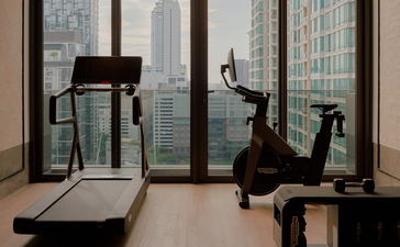 Fitness studio at Aman Nai Lert Bangkok with treadmill and exercise bike overlooking the city skyline.