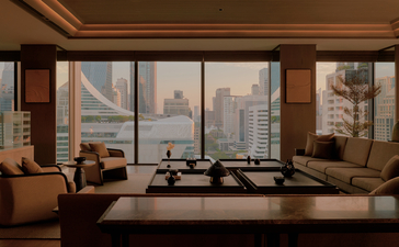 Aman Suite living room at Aman Nai Lert Bangkok with floor-to-ceiling windows overlooking the city skyline.