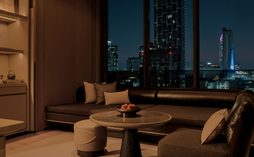 Aman Suite room at Aman Nai Lert Bangkok, with city views at dusk and contemporary furnishings.
