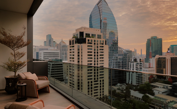 Aman Suite terrace overlooking Bangkok's skyline at dusk, with city buildings and warm golden light.