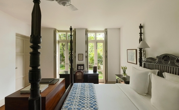 Garden bedroom at Amangalla with doors opening to greenery and patterned blue floor runner.