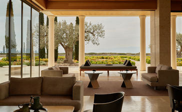 Resort bar and lounge at Amanzoe with floor-to-ceiling windows overlooking Greek countryside, neutral furnishings and natural light.