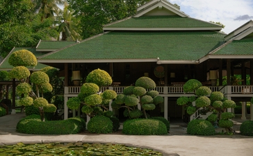 Traditional Thai pavilion with green roof at Aman Nai Lert Bangkok, surrounded by sculpted topiaries and mature trees.