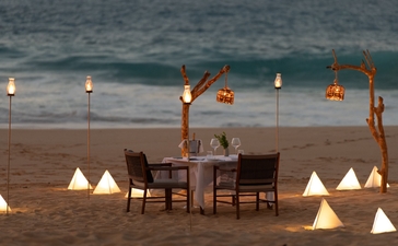 Cena privada en la playa de Amanera, con mesa junto al mar y velas iluminadas al atardecer.