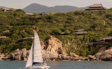 Catamaran sailing on turquoise waters off the Vietnamese coast near Amanoi, with forested hills and mountains in the background.