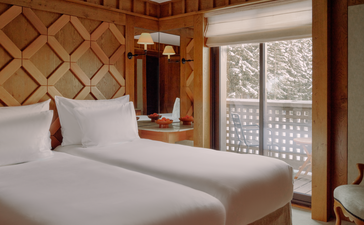 Junior family apartment bedroom at Aman Le Mélézin with twin beds and Alpine views through latticed windows.