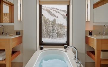 Bathroom at Aman Le Mélézin with soaking tub, wooden cabinetry and framed alpine landscape.