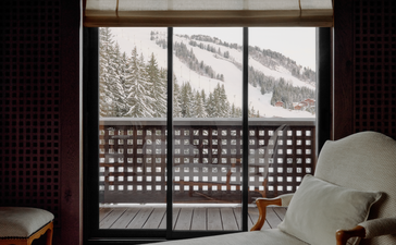 Bedroom window at Aman Le Mélézin with three framed mountain prints and wooden lattice shutters.