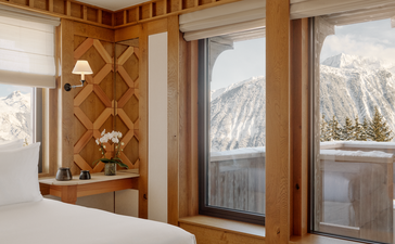 Chambre Nord bedroom at Aman Le Mélézin with wooden panelling, white bed, and alpine views through glass doors.