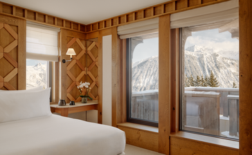 Chambre Nord bedroom at Aman Le Mélézin with wooden panelling, bed and mountain views through glass doors.