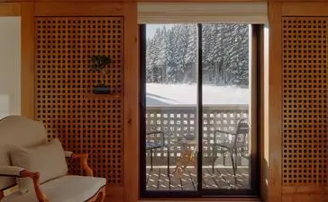 Ski piste-view bedroom at Aman Le Mélézin with wooden lattice cabinetry and snowy Alpine landscape visible through balcony doors.