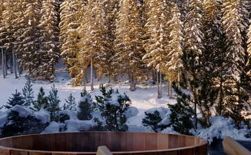 Wooden terrace overlooking snow-covered grounds and frost-laden pine forest at Aman Le Mélézin.