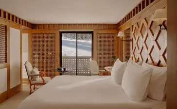 Ski-in bedroom at Aman Le Mélézin with wooden walls, two beds and mountain views through glass doors.