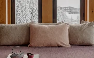 Chambre au resort Aman Le Mélézin avec coussins beiges et vue sur les montagnes enneigées.