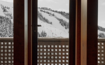 Wooden-framed windows with geometric lattice panels overlooking snow-covered Alpine slopes at Aman Le Mélézin.