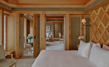 Suite bedroom at Aman Le Mélézin with cream bedding, wooden panelling, and geometric wall patterns.