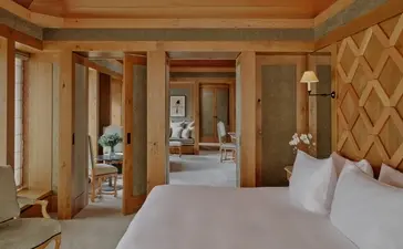 Suite Mélézin avec lit blanc et boiseries claires à Aman Le Mélézin, station de montagne française.