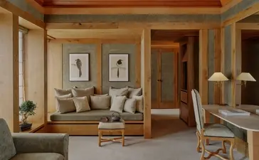 Suite Mélézin sitting area at Aman Le Mélézin resort, with cream furnishings and wooden panelling.