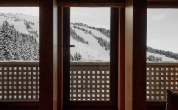 Wooden-framed windows at Aman Le Mélézin revealing snow-covered Alpine slopes beyond latticed screens.