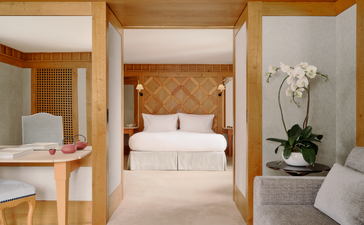 Accommodation suite at Aman Le Mélézin with wooden-framed bedroom doorway and white bedding visible beyond.