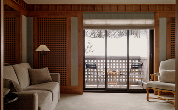 Accommodation suite at Aman Le Mélézin with seating area overlooking ski piste through balcony doors.